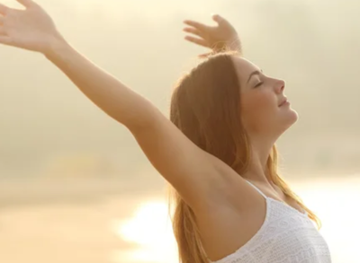 朝日の中で深呼吸しながら両手を広げてリラックスする女性