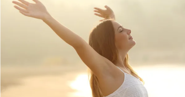 朝日の中で深呼吸しながら両手を広げてリラックスする女性