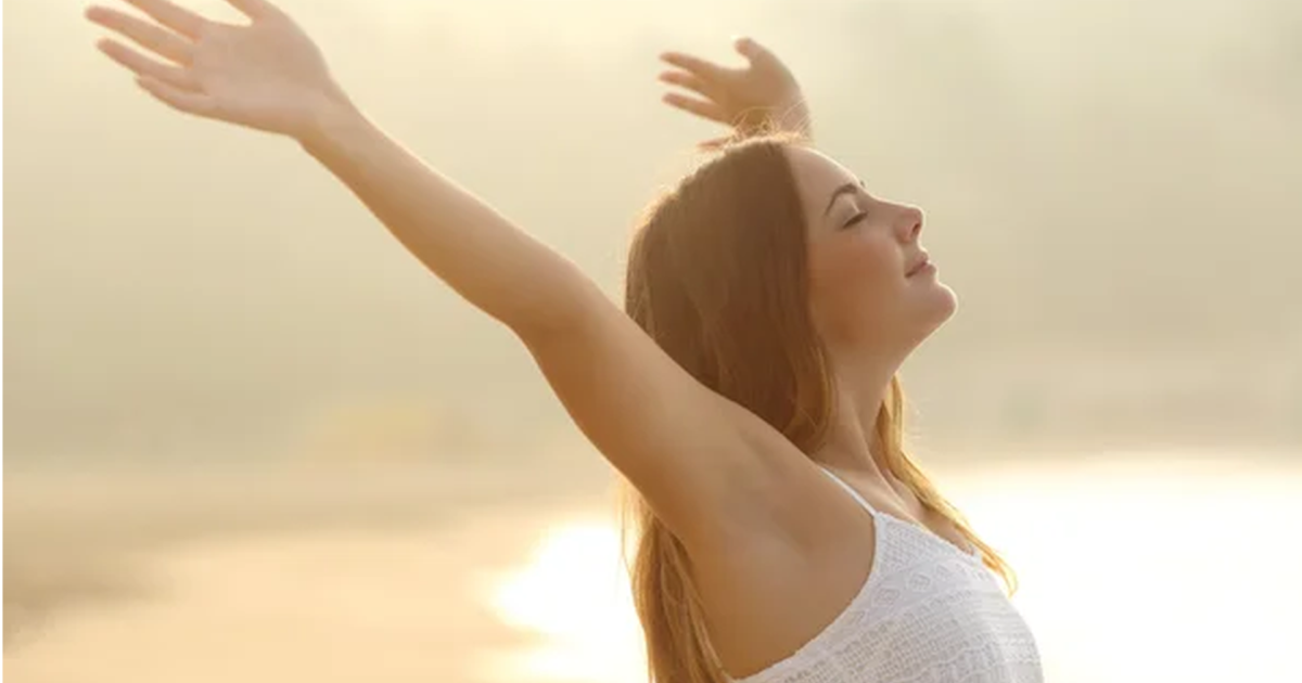 朝日の中で深呼吸しながら両手を広げてリラックスする女性