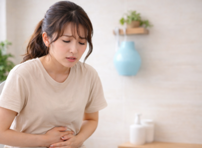 便座に座りお腹を押さえて悩む女性の様子（便秘や出ない不快感のイメージ）