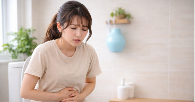便座に座りお腹を押さえて悩む女性の様子（便秘や出ない不快感のイメージ）